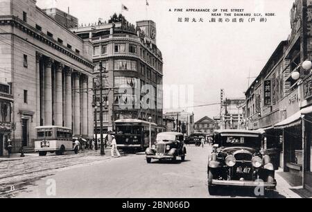 [ 1930 Giappone - Kobe Street View ] - Street view con auto, un tram e un autobus, vicino Motomachi (元町) strada dello shopping a Kobe, Prefettura di Hyogo. L'ampio edificio nel centro è Daimaru (大丸), grande magazzino, aperto nel 1927 (Showa 2). cartolina vintage del xx secolo. Foto Stock