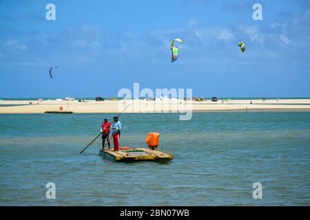 Due uomini che attraversano il fiume Ceara-mirim in una piccola barca e kite surfisti in background. Foto Stock