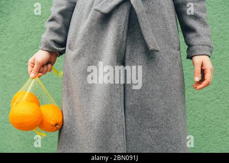 Donna tiene fresche Orange in plastica Mesh Sack su sfondo verde Foto Stock