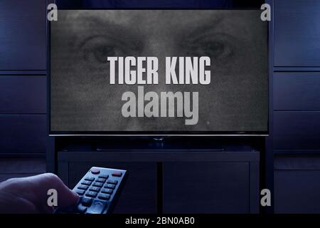 Un uomo punta un telecomando TV al televisore che visualizza la schermata principale del titolo di Tiger King (solo per uso editoriale). Foto Stock