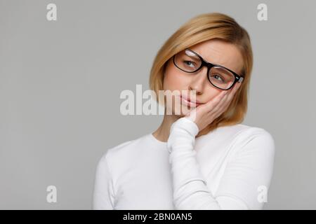 Donna dispiaciuta quasi addormentata al lavoro, tieni la testa con la mano. Lo studente assonnato che trascorre il tempo all'università, sente la mancanza di energia. Dormire in modo da non dormire Foto Stock