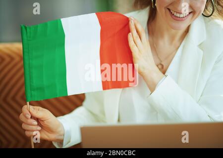 Primo piano su donna sorridente con computer portatile e bandiera italiana imparare la lingua straniera nel soggiorno in giorno di sole. Foto Stock