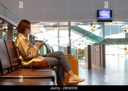 Donna sconvolto sopra la cancellazione del volo, scrive il messaggio alla famiglia, seduto in un terminal quasi vuoto aeroporto a causa di coronavirus pandemic/Covid-19 focolaio Foto Stock