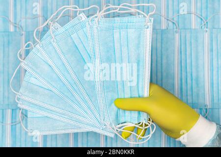 Medico che tiene in mano le maschere chirurgiche blu per il viso in guanto protettivo giallo. Immagine di concetto sullo sfondo di bende respiratorie di gruppo per Foto Stock