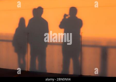 I visitatori gettano ombre sulle pareti dell'osservatorio Griffith Park al tramonto mentre ammirano lo skyline di Los Angeles, California, Stati Uniti, colore Foto Stock