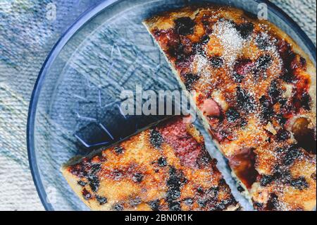 torta fatta in casa a pezzi di semplice biscotto di frutti di bosco fatta di lamponi e fragole cosparsa di zucchero su una piastra rotonda di vetro blu trasparente su un blu Foto Stock