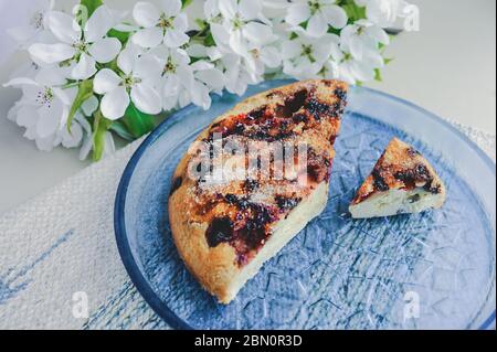 torta fatta in casa a pezzi di semplice biscotto di frutti di bosco fatta di lamponi e fragole cosparsa di zucchero su una piastra rotonda di vetro blu trasparente su un blu Foto Stock