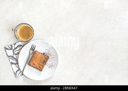 Vista dall'alto di una tazza di caffè e un piatto da dessert con torta di brownie su sfondo rustico bianco. Foto Stock