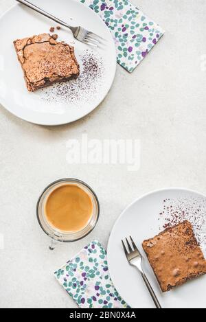 Vista dall'alto di una tazza di caffè e due piatti da dessert con torta di brownie su sfondo rustico bianco. Foto Stock