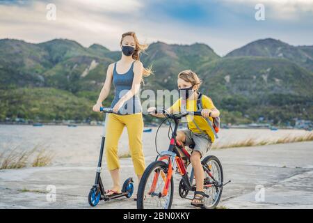 Ragazzo scuola attiva e la sua mamma in maschera medica a cavallo di una bicicletta con zaino in giornata di sole. Buon bambino in bicicletta sulla strada per la scuola. È necessario andare a. Foto Stock
