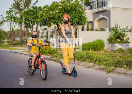 Bambino ragazzo scuola attiva e la sua mamma in maschera medica e casco di sicurezza in bicicletta con zaino in giornata di sole. Buon bambino in bicicletta sulla strada per la scuola. Tu Foto Stock