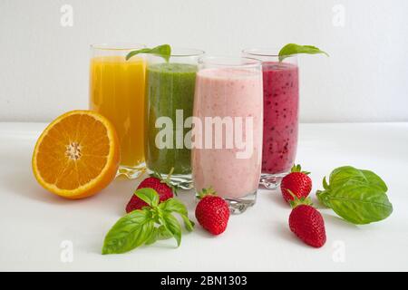Frullati colorati in vetro con frutta fresca su un tavolo bianco Foto Stock