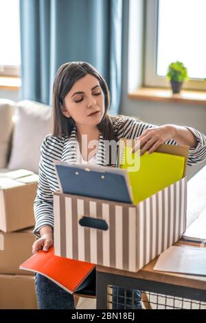 Giovane donna in una giacca a righe che impacchettano documenti e che guarda concentrato Foto Stock