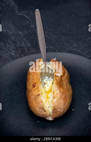 Patate al forno con una forchetta e burro su un piatto nero Foto Stock