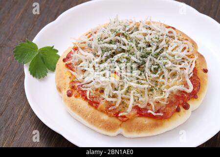 piccola pizza di shirasu di pesce su un piatto con tavolo di legno