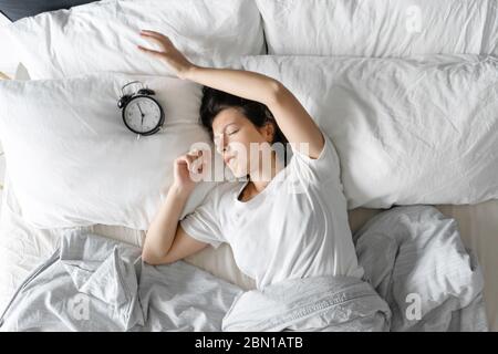 Vista dall'alto. La ragazza dorme accanto alla sveglia. Tentativo di disattivare la sveglia che interferisce con la modalità di sospensione. Tempo di attivazione. Profondo Foto Stock