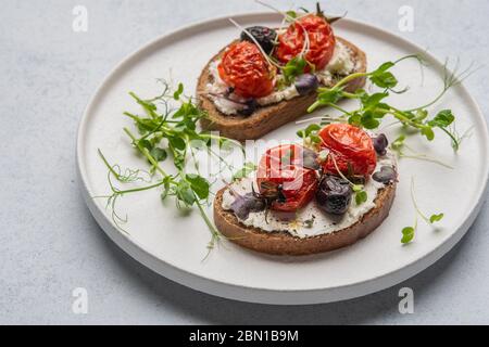 Panini con pomodori, olive, formaggio ed erbe al forno su un piatto bianco in ceramica Foto Stock