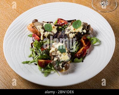 Crostini con funghi della foresta saltati, aglio, basilico e mozzarella. Tradizionale antipasto italiano su rucola, insalata di foglie di aragola. Foto Stock