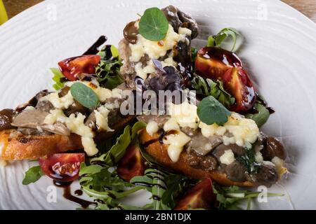 Crostini con funghi della foresta saltati, aglio, basilico e mozzarella. Tradizionale antipasto italiano su rucola, insalata di foglie di aragola. Foto Stock