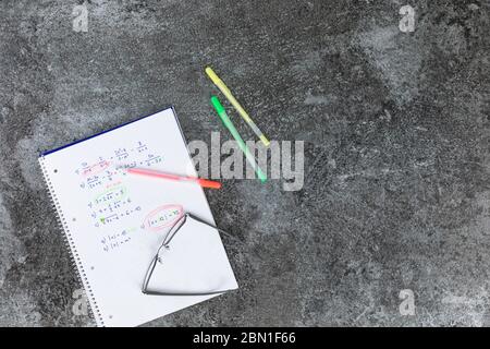 Libro di matematica scritto a mano con problemi aritmetici, vetri di lettura aperti con matita arancione, gialla e verde Foto Stock