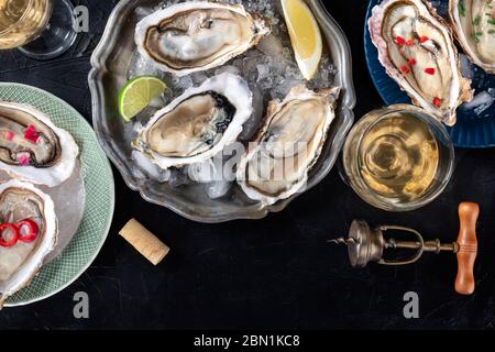 Ostriche con vari condimenti, sparate dall'alto con vino, con limone e lime, pepe, cipolla, su fondo scuro con un posto per il testo Foto Stock