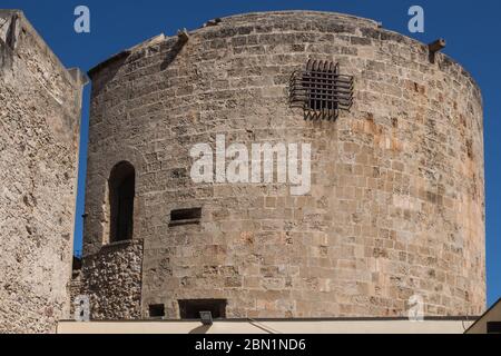 Costruzione circolare della torre di fortificazione in pietra con piccole finestre. Cielo blu brillante. Alghero, Sardegna, Italia. Foto Stock