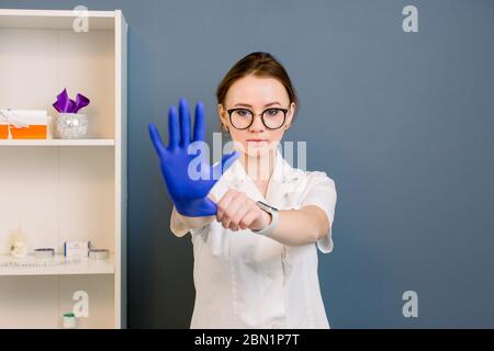 Giovane attraente dottore donna che mostra mano in guanto medico blu, in centro termale, medico. Ritratto di donna che indossa divisa medica e guanti in Foto Stock