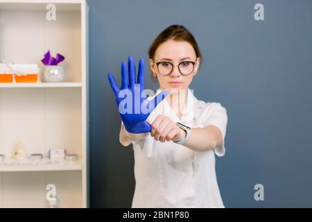 Giovane attraente dottore donna che mostra mano in guanto medico blu, in centro termale, medico. Ritratto di donna che indossa divisa medica e guanti in Foto Stock