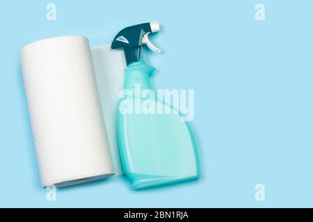 Un rotolo di carta da cucina e un flacone spray per la pulizia su sfondo azzurro Foto Stock