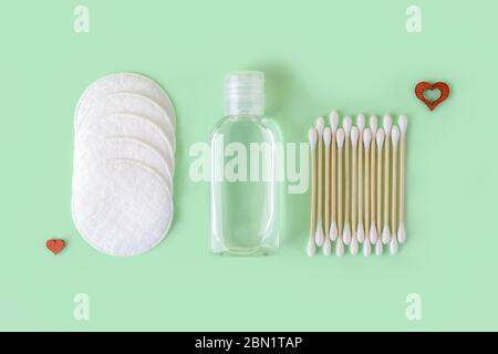 Lozione detergente o tonico in un vaso trasparente, tamponi di cotone e bastone di legno boccioli di cotone su uno sfondo di menta pastello. Concetto di materiali ecocompatibili Foto Stock