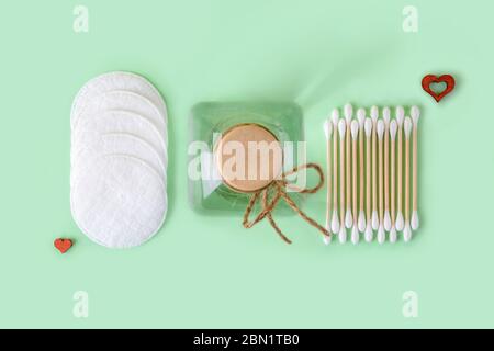 Lozione o tonico detergente in un vaso di vetro, tamponi di cotone e bastone di legno di cotone gemme su uno sfondo color menta pastello. Concetto di materiali ecocompatibili. Foto Stock
