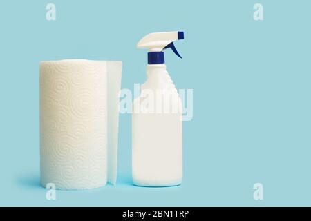 Un rotolo di carta da cucina e un flacone spray per la pulizia su sfondo azzurro Foto Stock
