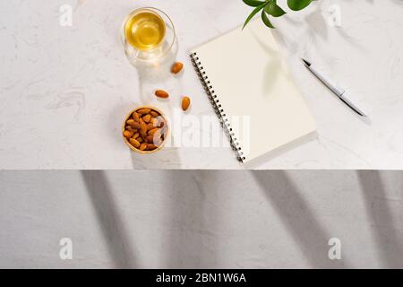 Flatlay di taccuino, macaron torta, tazza di tè e foglie su tavola bianca Foto Stock