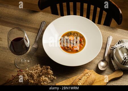 Un piatto profondo di lenticchie stufate e un bicchiere di vino su un tavolo di legno Foto Stock