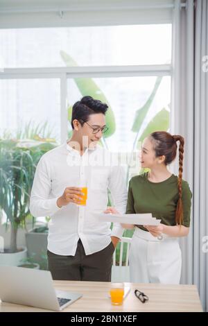 Adorabile coppia sorridente bonding durante il lavoro e bere succo d'arancia in luminoso caldo giorno di sole Foto Stock