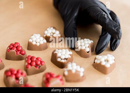 Primo piano cioccolatini a forma di cuore con ripieno rosso in mani di pasticceria donna su sfondo cucina Foto Stock