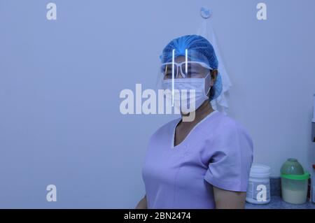 Protezione totale, ritratto di un assistente dentale cambogiano, un operaio di frontline, indossando una maschera protettiva del viso, visiera di protezione e rete per capelli (PPE) in una clinica dentale durante la pandemia del coronavirus. Phnom Penh, Cambogia. © Kraig Lieb Foto Stock