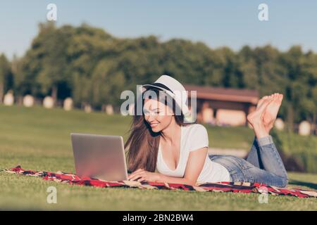 Rinfrescharsi al sole. Così comodo e facile! Giovane ragazza felice sta scrivendo nel suo laptop che giace sulla plaid sull'erba al parco in primavera all'aperto Foto Stock