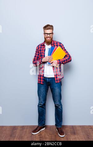 Allegro giovane nerdy rosso barbuto studente in piedi con libri su sfondo puro in occhiali e abbigliamento casual Foto Stock