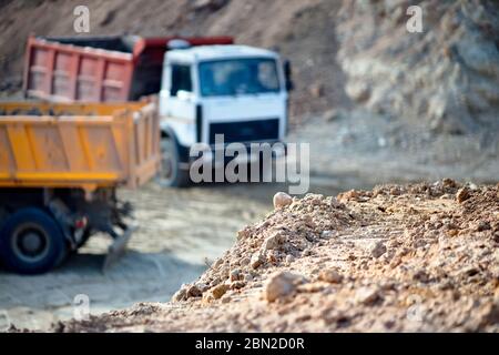 Mucchio di rocce di minerale su sfondo sfocato con due pesanti camion minerari multi-ton che esportano minerali da miniera a cielo aperto. Concetto di spedizione Foto Stock