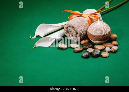 Essenziale per il centro benessere, candela, pietre, asciugamano e fiori su sfondo verde scuro Foto Stock