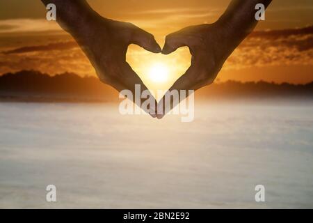 silhouette di mani a forma di cuore contro il tramonto cielo. Foto Stock