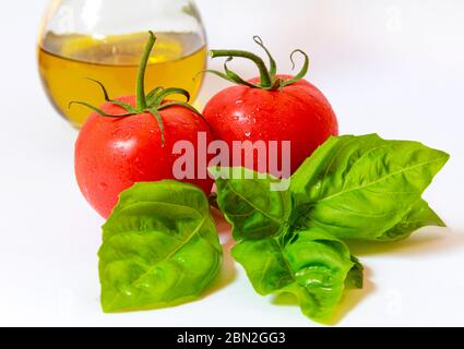 Due pomodori maturi con steli, un rametto di basilico fresco e una cruetta di olio d'oliva isolata su bianco. Foto Stock