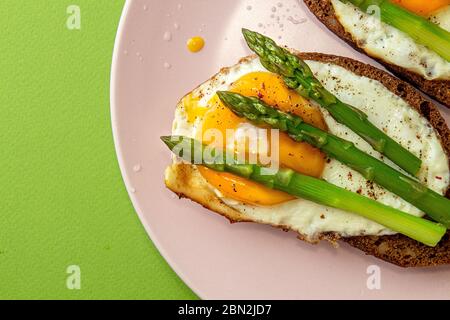 Toast deliziosi panini con asparagi e uova fritte su piatto rosa su sfondo verde. Vista dall'alto, spazio per fotocopie Foto Stock