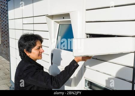 Donna asiatica britannica che utilizza un armadietto postale automatico, punto di raccolta pacchi nel Regno Unito Foto Stock