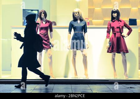 Giovane donna che passa per manichini in piedi in una vetrina Foto Stock