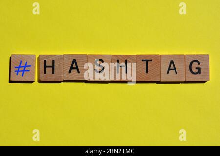 Hashtag, parola e simbolo in lettere in blocco di legno su sfondo giallo brillante Foto Stock