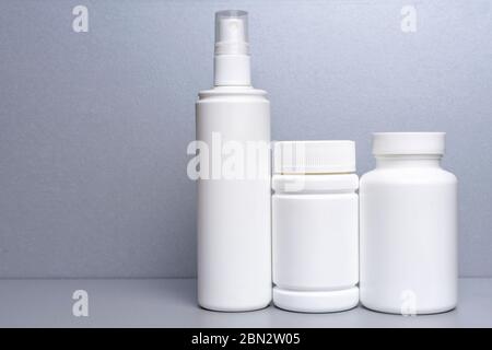 3 contenitori di plastica per medicinali e vitamine, una bottiglia con spruzzatore su fondo grigio. lattine bianche senza nome Foto Stock