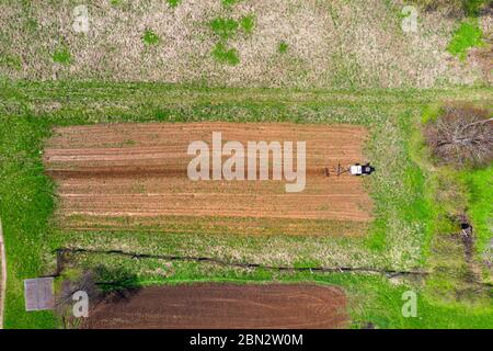 Il trattore aratri un piccolo campo nel villaggio prima di piantare verdure. Vista dell'altezza dell'antenna Foto Stock