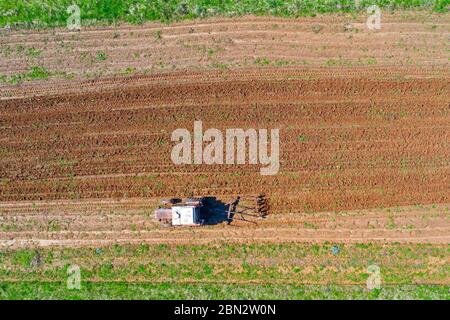 Il trattore aratri un piccolo campo nel villaggio prima di piantare verdure. Vista dell'altezza dell'antenna Foto Stock